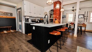 A kitchen with a central island, bar stools, a brick accent wall, and pendant lighting. - Little House on Taylor - 2 Bedroom Cottage in Walkable Downtown Location (Craig)