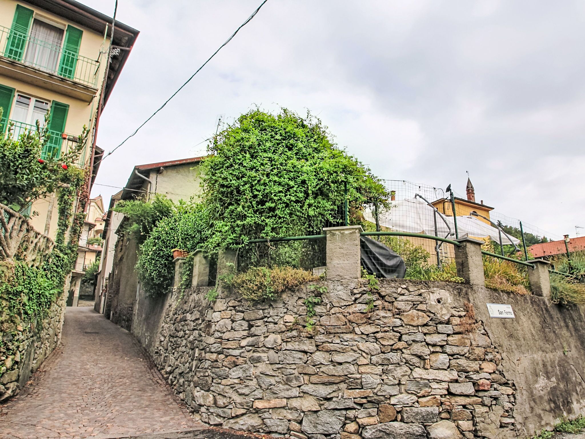 A narrow stone pathway leading to a building with a stone wall and a metal fence.