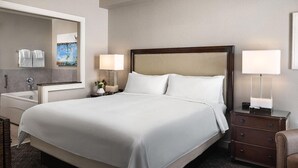 Habitación de hotel con una cama grande, lámparas de noche, mesita de noche, un espejo y vistas al baño.