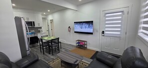 Ein modernes Wohnzimmer mit Essbereich, einer Küche mit weißen Schränken, einem Flachbildfernseher und einem Schuhregal.