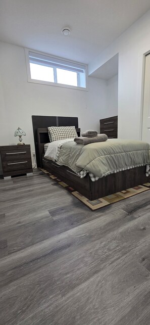 Un dormitorio con cama, mesita de noche, lámpara y ventana.
