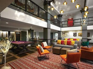 Eine mehrstöckige Hotelhalle mit Billardtisch, Sitzgelegenheiten und einer Treppe.