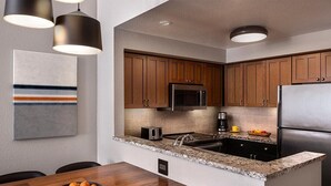 Una cocina moderna con armarios de madera, un refrigerador de acero inoxidable, un microondas y una encimera de granito.