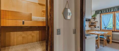 Una habitación con una cama individual superpuesta, un espejo, un radiador, una mesa con sillas y una ventana con cortinas.