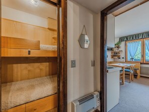 A room with a bunk bed, a mirror, a radiator, a table with chairs, and a window with curtains. - Presanella by Interhome (Madonna di Campiglio)