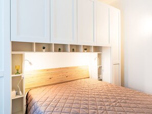 Ein Schlafzimmer mit einem Holz-Kopfteil, einem Bett mit gesteppter Bettdecke, weißen Schränken mit Regalen und einem Nachttisch mit Lampe.