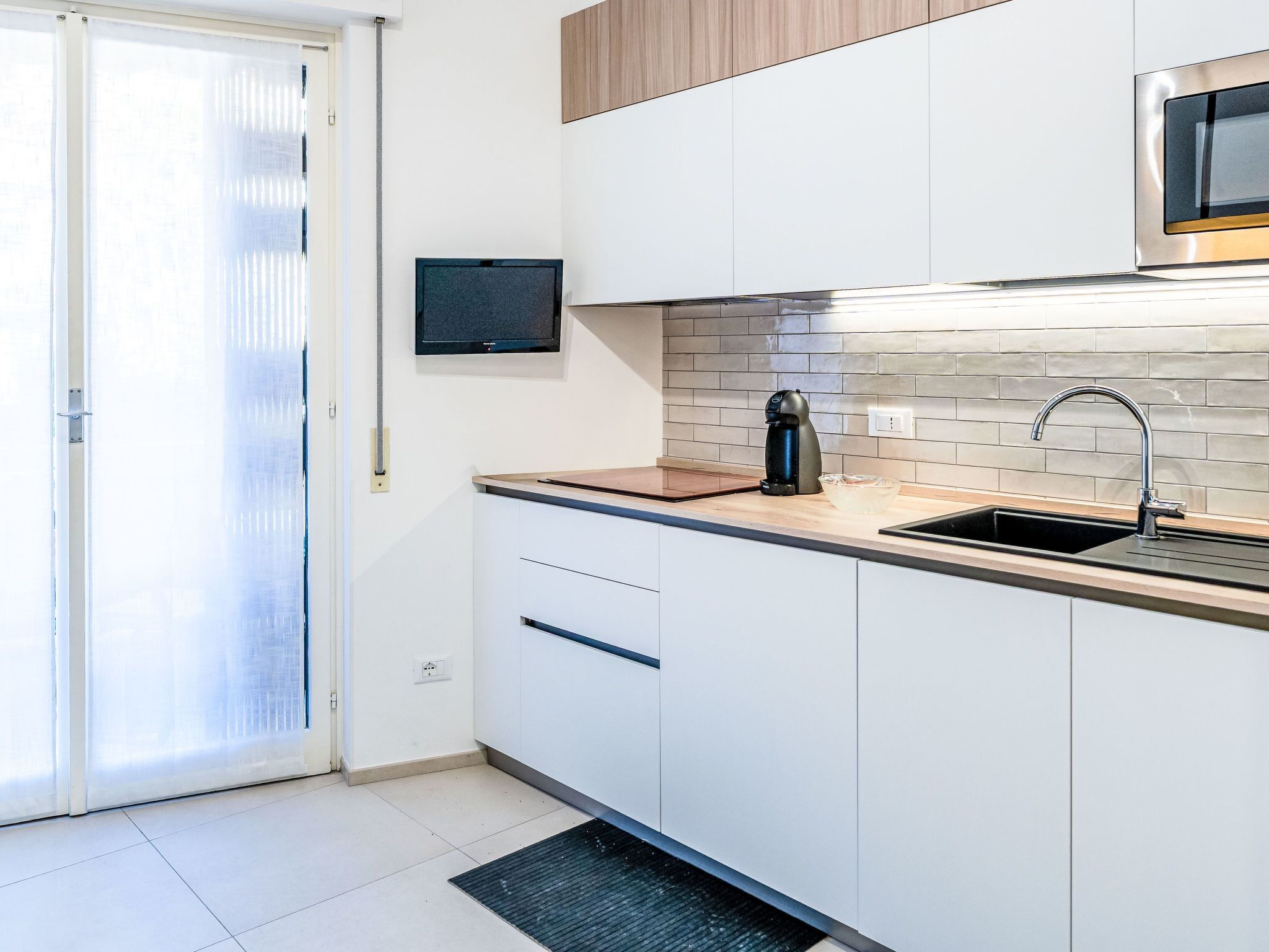 A modern kitchen with a coffee maker, a sink, and a television on the wall.