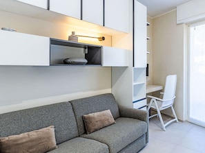 A modern living room with a grey sofa, a white chair, and built-in shelving with decorative items. - Casa Letizia by Interhome (Sanremo)