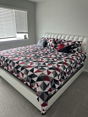 A bed with a geometric patterned bedspread, a tufted headboard, and a window with blinds. - Charming townhome in gorgeous Milliken Colorado with easy access to relaxation . (Milliken)