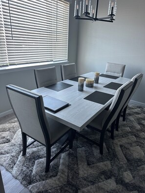 A dining room with a rectangular table, six chairs, a chandelier, and a window with blinds. - Charming townhome in gorgeous Milliken Colorado with easy access to relaxation . (Milliken)