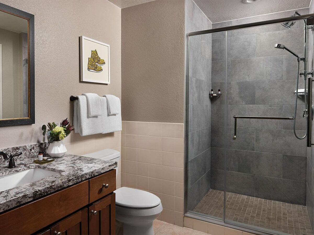Une salle de bain avec un lavabo en marbre, des toilettes, une douche avec une porte en verre et un tableau encadré au mur.