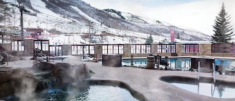 A spa area with hot tubs and a pool, surrounded by stone structures and a snowy mountain backdrop.