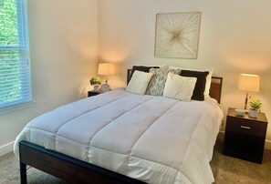 A neatly made bed with a white duvet, two bedside tables with lamps, a wall art piece, and a window with blinds. - Quiet, gated, near Towncenter Market st (Spring)