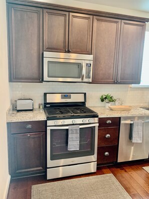 A kitchen with dark wood cabinets, a stainless steel microwave, a gas stove, and an oven. - Quiet, gated, near Towncenter Market st (Spring)