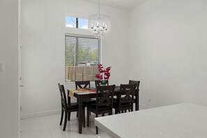 Uma área de refeições com mesa, cadeiras, uma janela com persianas e um candelabro.