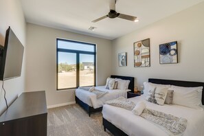 A bedroom with two beds, a ceiling fan, artwork on the walls, and a large window. - Apache Junction Vacation Rental Heated Pool, Mountain Views, Pet-Friendly Home (Apache Junction)