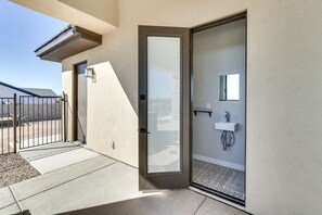 A modern building entrance with a sliding glass door, a small outdoor seating area, and a visible bathroom with a sink and mirror. - Apache Junction Vacation Rental Heated Pool, Mountain Views, Pet-Friendly Home (Apache Junction)