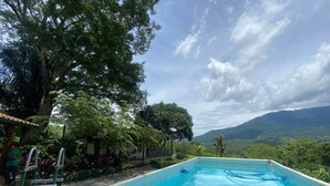 A rectangular pool with clear blue water, surrounded by lush greenery and trees, with a mountainous landscape in the background. - 2-bedroom private Oasis 1 hour from airport with AC - Pool, views and privacy. (San José)