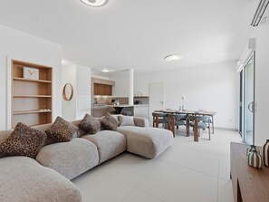 A modern living room with a sectional sofa, a dining area with a table and chairs, and a kitchen in the background.