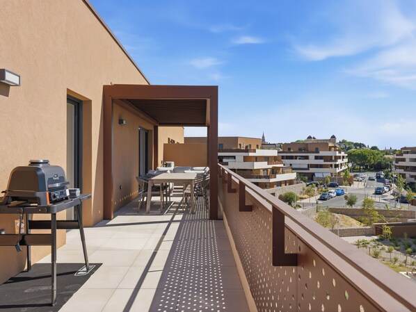 A balcony with a grill, outdoor furniture, and a view of surrounding buildings.