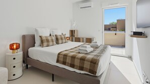 Ein modernes Schlafzimmer mit einem Bett, Nachttischen, einem Fernseher und Blick auf einen Balkon.