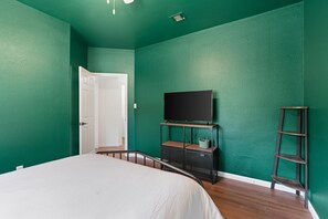 Ein Schlafzimmer mit einem Bett, einem Fernseher auf einem Schrank, einer Tür und einem Regal mit einem Korb.