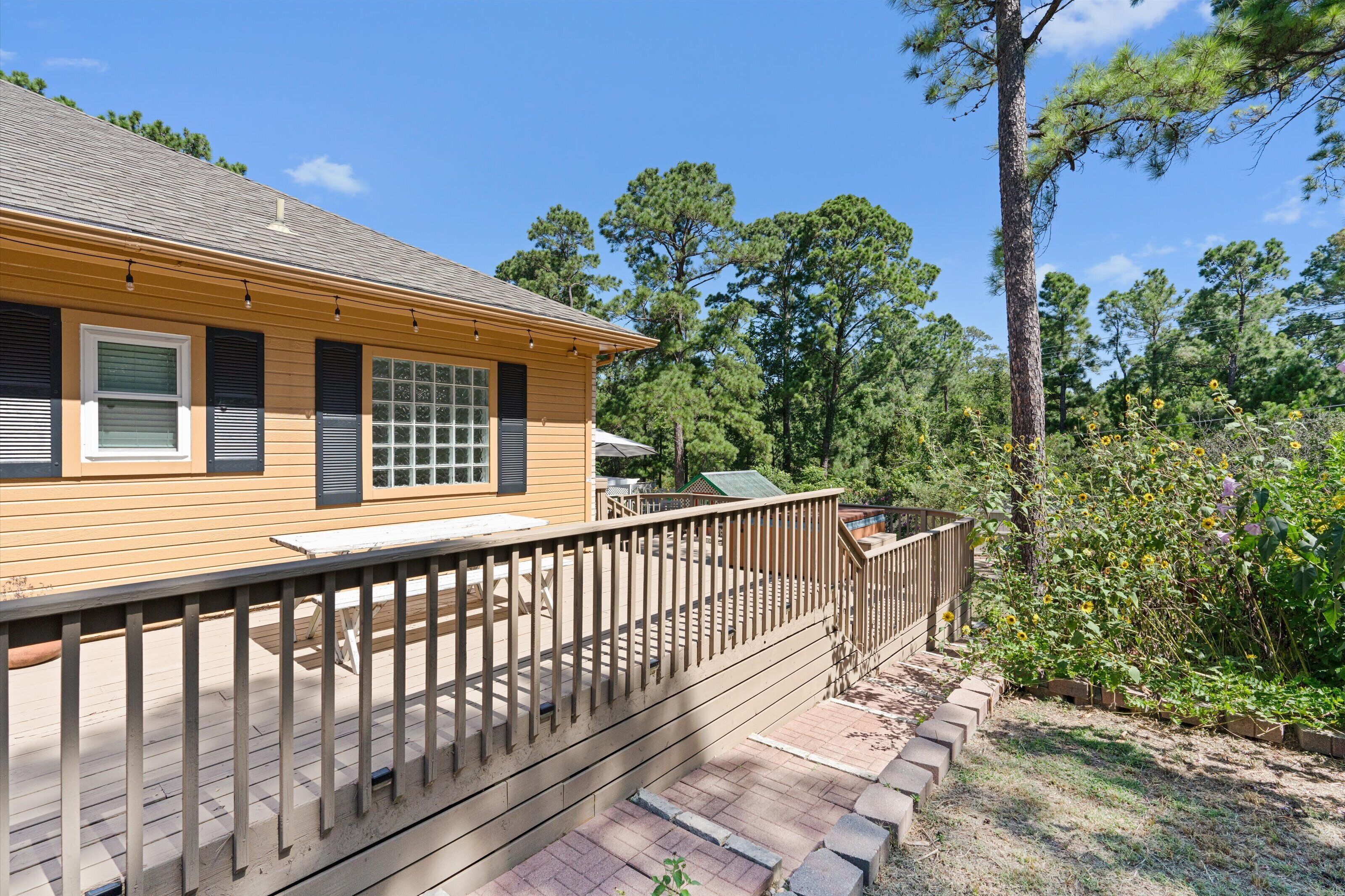 A wooden house with a deck, a covered patio, and a garden with yellow flowers.
