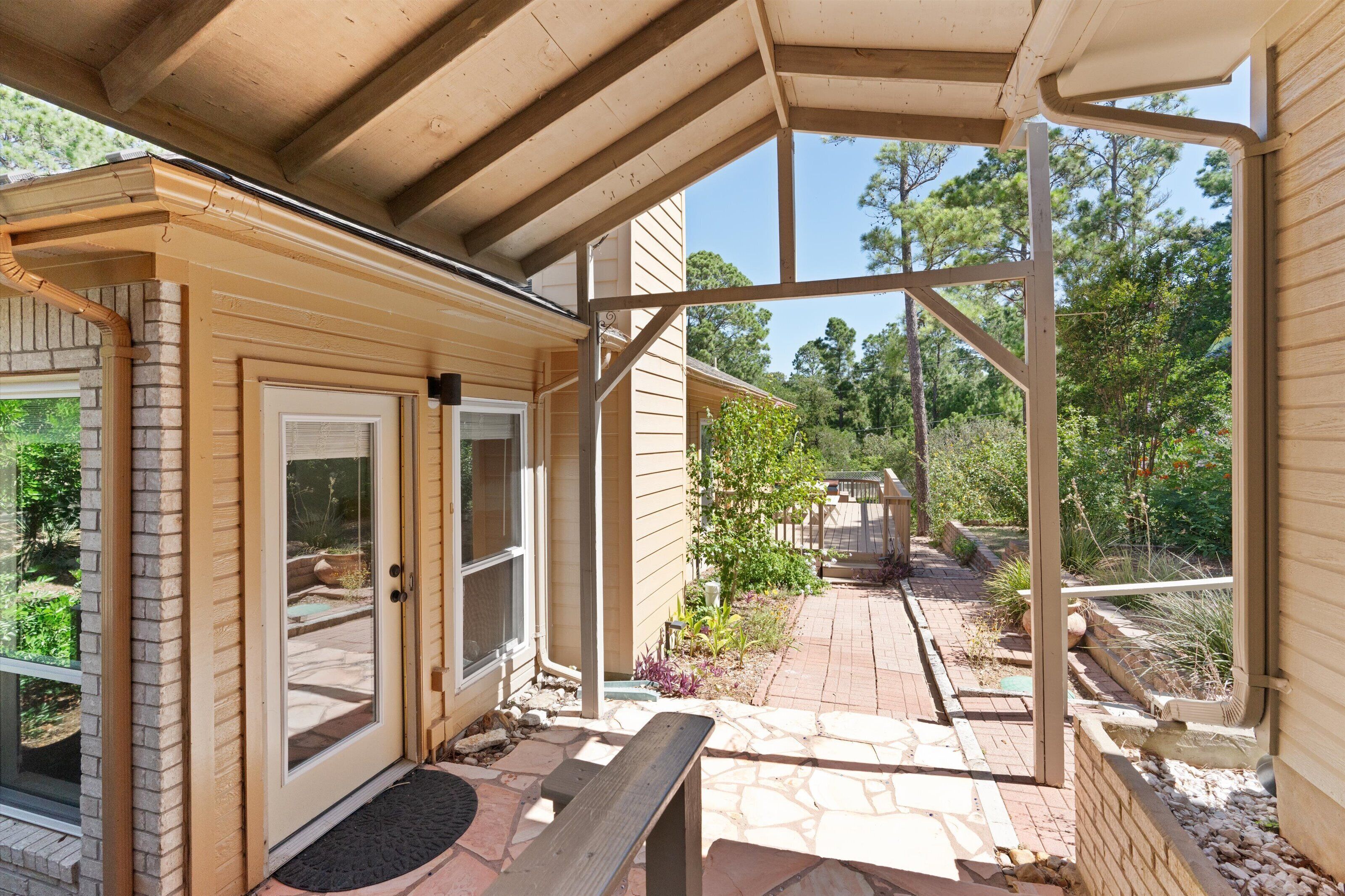 A covered outdoor area with a wooden bench, a door with a screen, and a stone pathway leading to a garden.