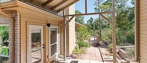 A covered outdoor area with a wooden bench, a door with a screen, and a stone pathway leading to a garden.