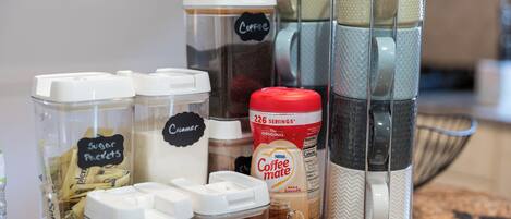 Eine Küchenarbeitsplatte mit verschiedenen Kaffeuzubereitungsmitteln, darunter Zuckerportionen, Sahne und eine Kaffeemaschine.