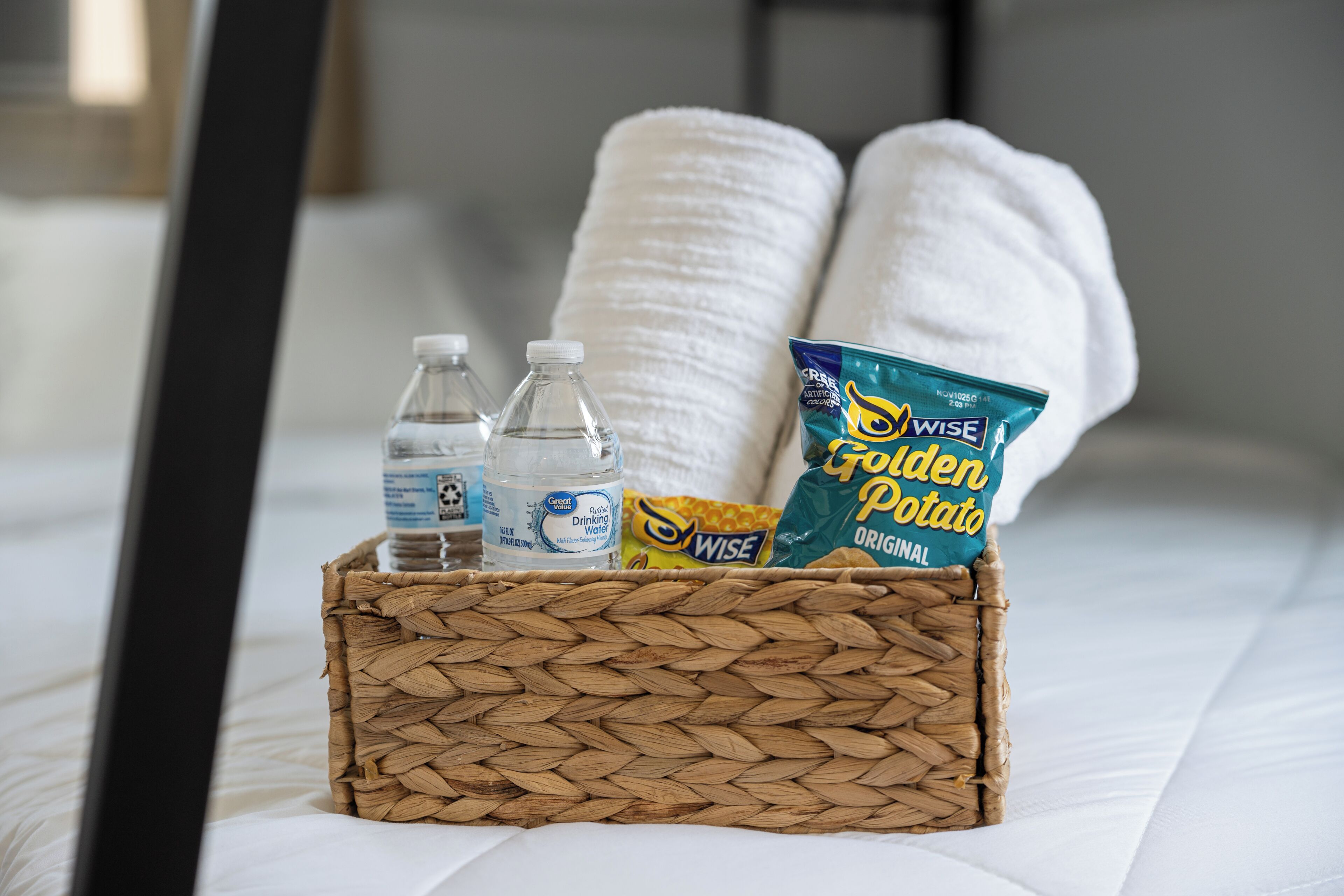 Un panier contenant une bouteille d’eau, une serviette et un paquet de collations, posé sur un lit.