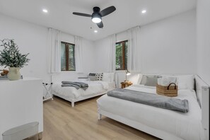 Une chambre moderne avec deux lits, un ventilateur de plafond et de grandes fenêtres.