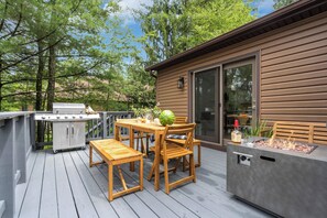 Una terraza de madera con una parrilla, una mesa con sillas y una chimenea.