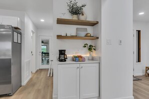 Une cuisine moderne avec des meubles blancs, un réfrigérateur en acier inoxydable, une machine à café et des plantes décoratives.