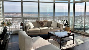 A spacious living area with a large window, a sofa, a coffee table, and a view of the cityscape. - Sundrenched 2 BDRM waterfront gem with lake view near CNE, BMO Field (Toronto)