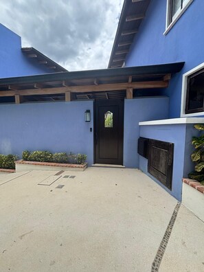 A building with a blue exterior, a wooden pergola, a black door, and a small garden area with plants. - 4BR Luxury Villa, Private Pool + Terrace in Las Catalinas (Guanacaste Province)