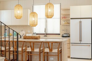 A modern kitchen with a central island, stainless steel appliances, and wicker pendant lighting. - 4BR Luxury Villa, Private Pool + Terrace in Las Catalinas (Guanacaste Province)