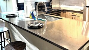 A modern kitchen with stainless steel appliances, a large island with stools, and wooden cabinetry. - Cozy 1-bedroom apartment in serene Atlanta with fitness room (Atlanta)