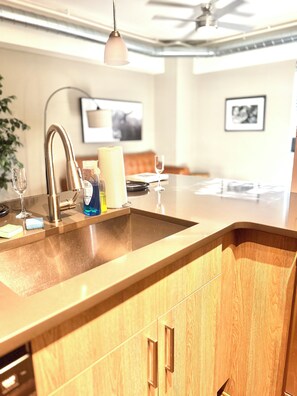 Eine Küche mit modernem Design, ausgestattet mit einem Edelstahlspülbecken, Holzschränken und einem Deckenventilator.