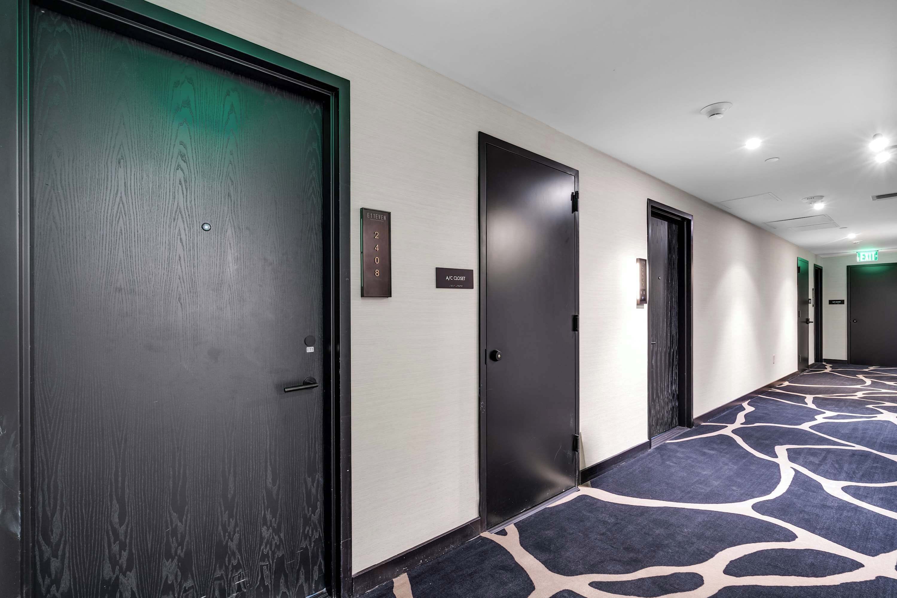 Pasillo de hotel con alfombra estampada, puertas oscuras y un cartel con los números de las habitaciones.