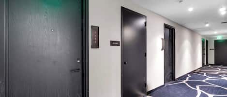 Pasillo de hotel con alfombra estampada, puertas oscuras y un cartel con los números de las habitaciones.