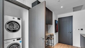 A modern laundry room with stacked washers and dryers, a bar stool, and a dark door. - Miami Pulse With Resort Amenities (Miami)