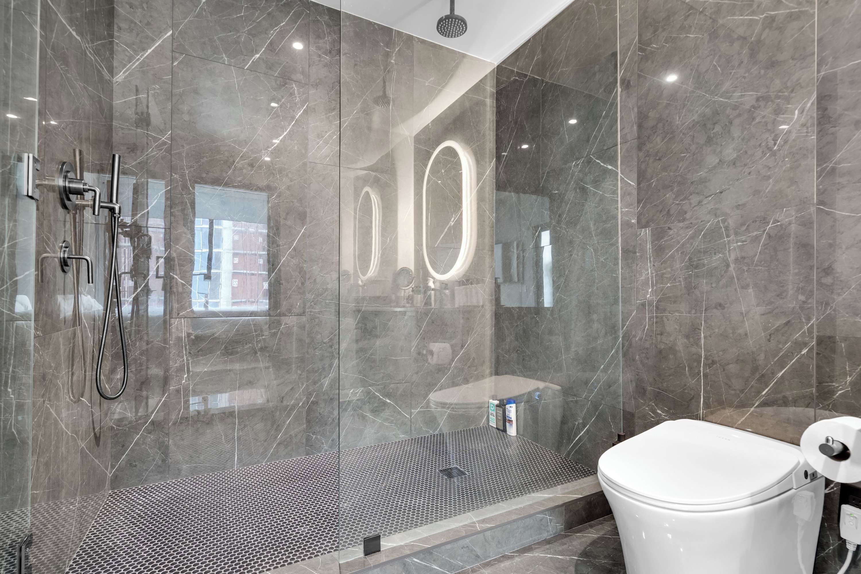 A modern bathroom with a glass-enclosed shower, a white toilet, and a marble-tiled wall.