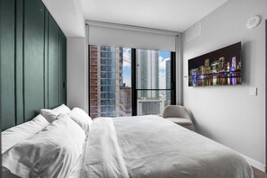 A modern bedroom with a bed, a chair, and a cityscape view through large windows. - Miami Pulse With Resort Amenities (Miami)