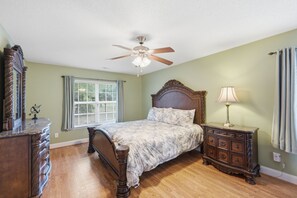 A bedroom with a bed, dresser, nightstand, lamp, ceiling fan, window with blinds, and a mirror. - Welcome to The Amsterdam Place. (Madison)