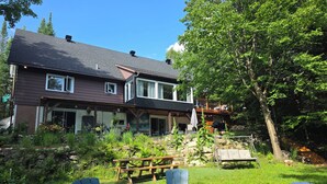 A two-story house with a patio area, outdoor seating, and a wooden deck.