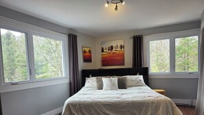 A bedroom with a large bed, two windows, a ceiling light, and a painting on the wall.
