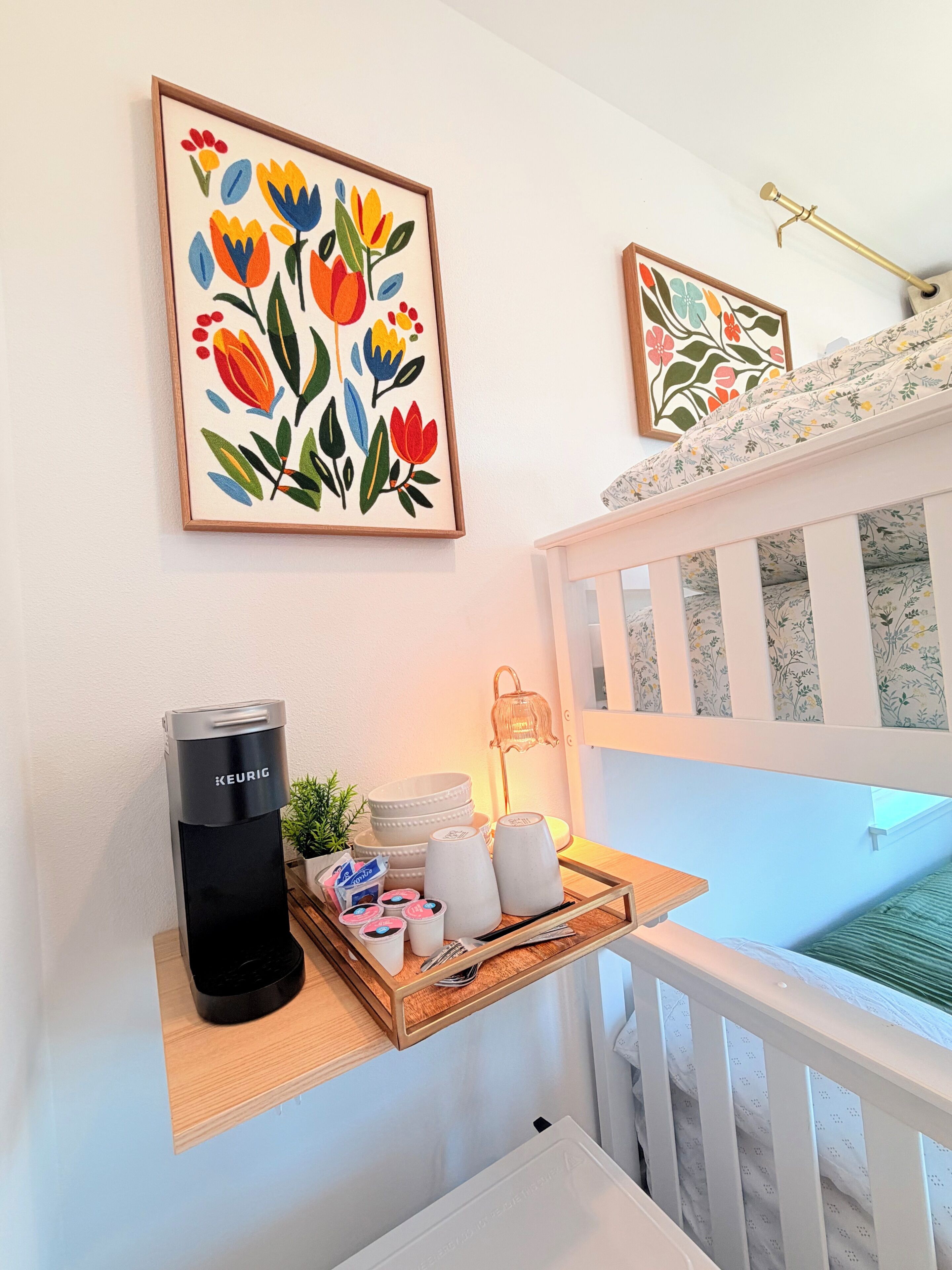 Una habitación con cafetera, una bandeja con tazas y una planta, y dos obras de arte florales enmarcadas en la pared.