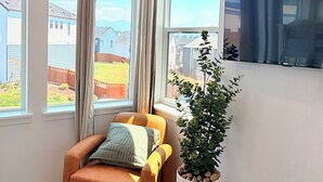 A modern living room with a sofa, a potted plant, and a television mounted on the wall. - Cozy Ensuite Room Near Mt. Rainier & Seattle (Bonney Lake)