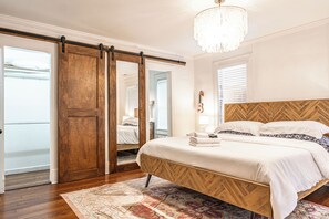 A bedroom with a bed, a chandelier, a wooden headboard, and a sliding door. - NEW! Downtown Charmer- Steps to downtown SoPines! (Southern Pines)